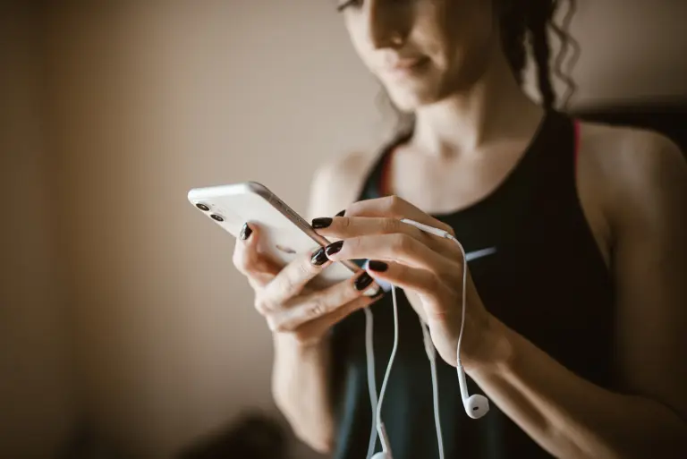 Woman using smartphone while listening to music in a fitness setting during the day